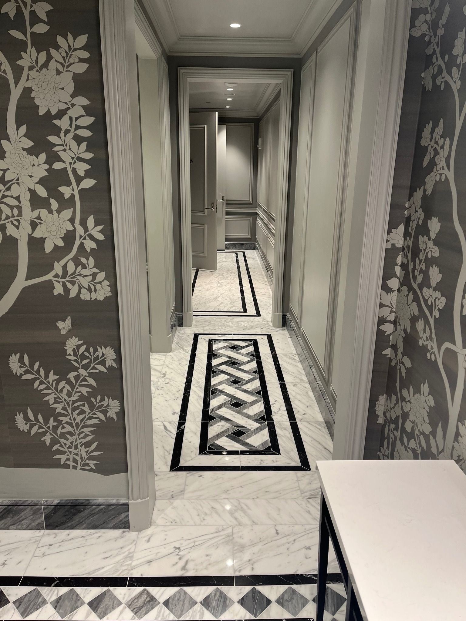 Narrow hallway with patterned wallpaper, carpet runner, and a white table in the foreground