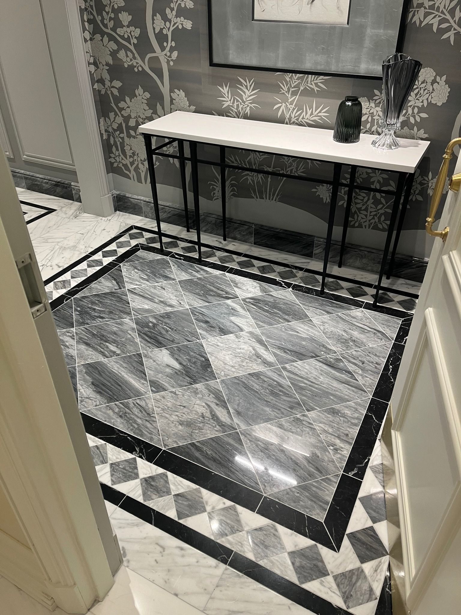 Modern bathroom with gray patterned rug, black console table, and white vanity at the far wall.