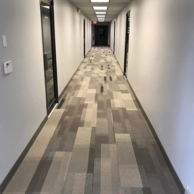 Long office hallway with white walls and gray patterned carpet, viewed from one end.