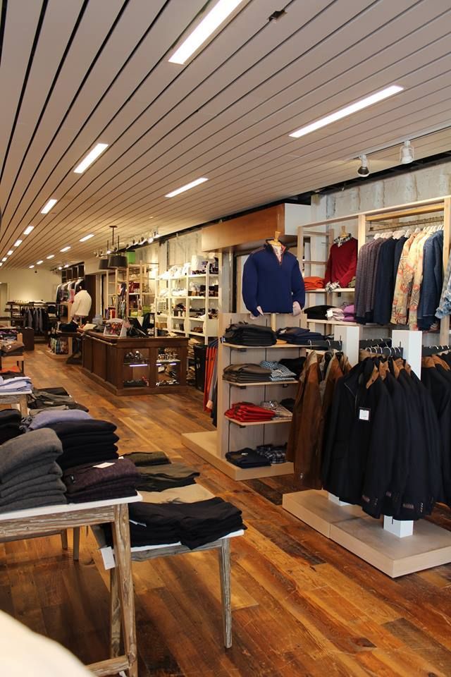 Clothing boutique interior with racks of folded sweaters, hanging jackets, and wooden floors