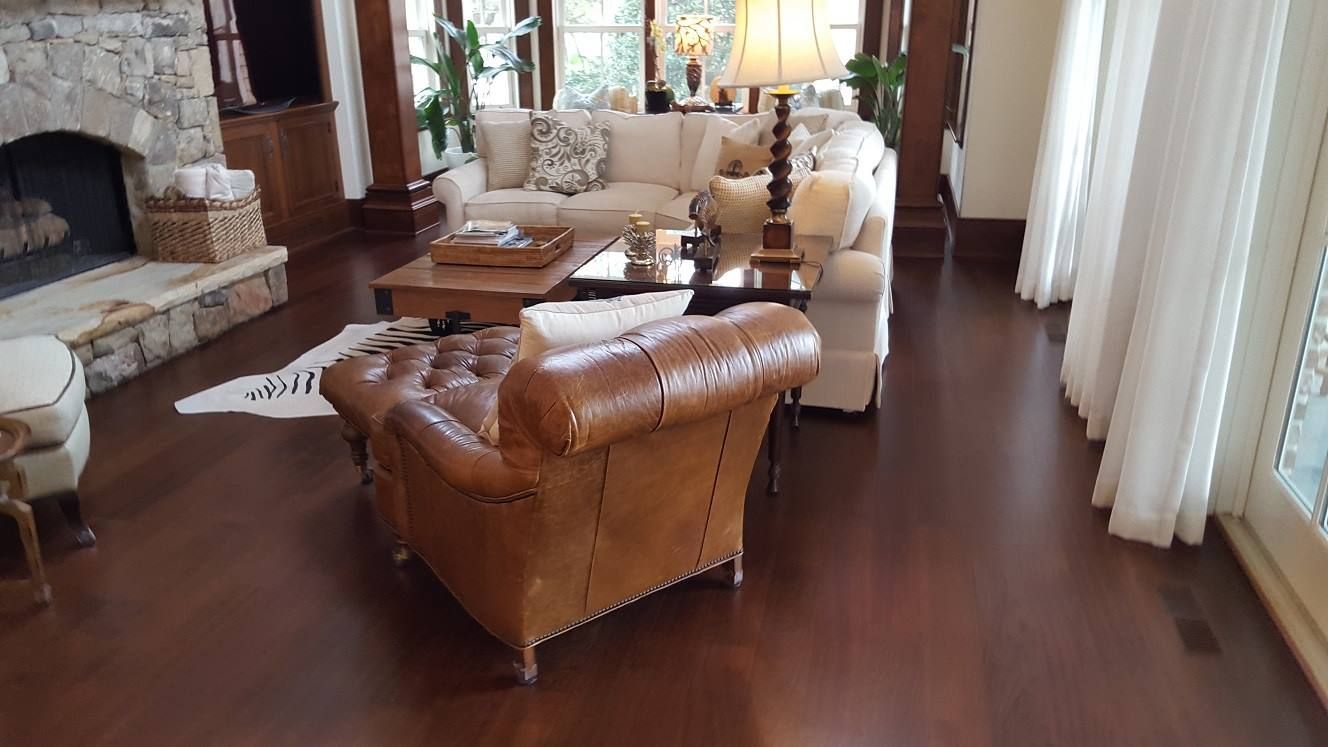 Warm living room with leather armchair, beige sofa, stone fireplace, and dark hardwood floors.