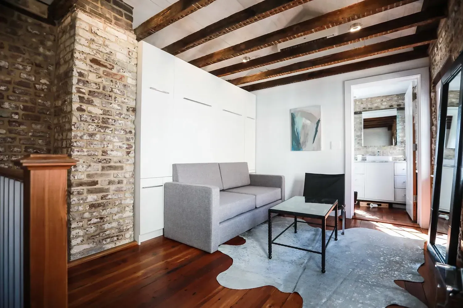 Loft living room with exposed brick, wooden beams, gray sofa, coffee table, and large mirror.