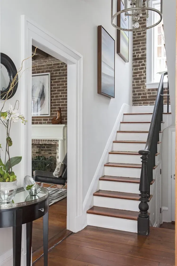 Bright entryway with staircase, white walls, wood floors, and a mirror by the stairs