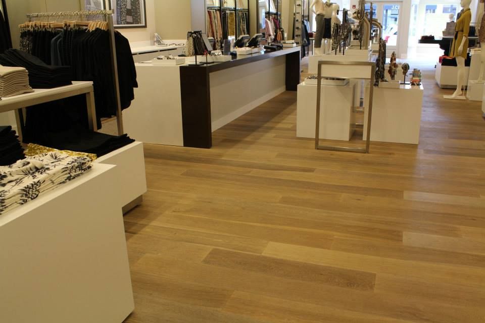 Clothing store interior with wooden floor, display tables, racks, and checkout counter