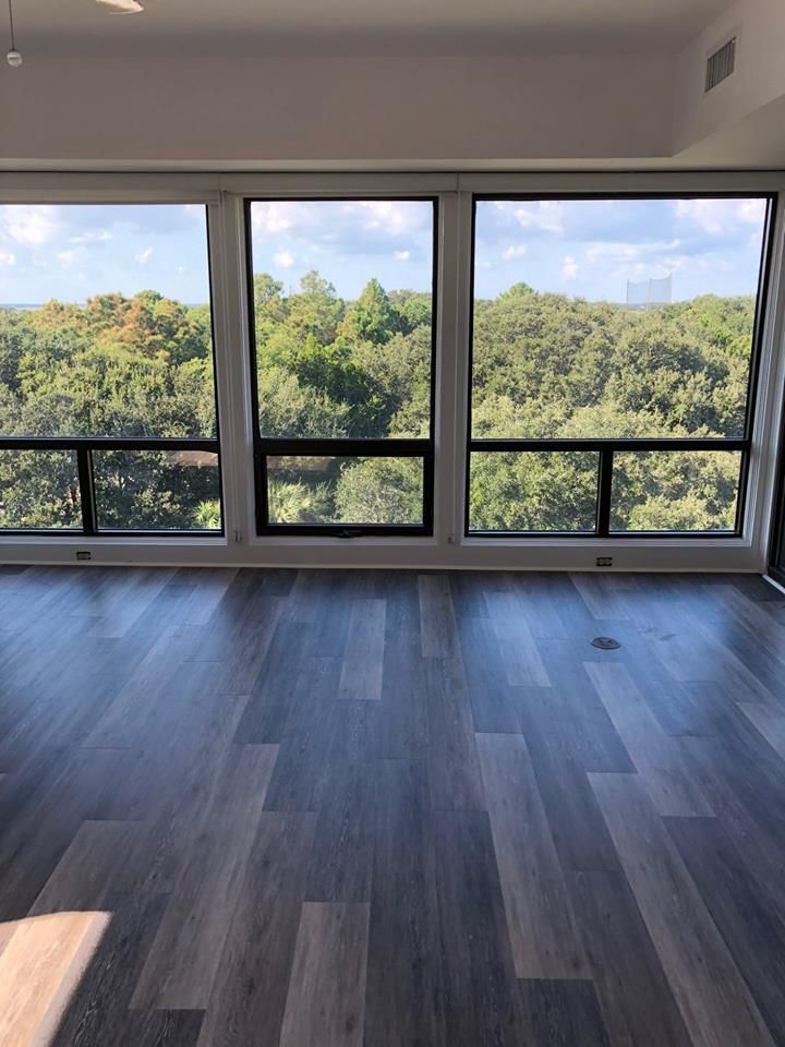 Empty modern room with dark wood floors and large windows overlooking green trees.