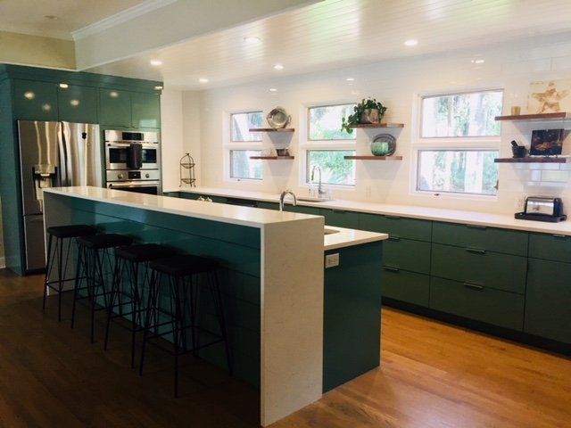 Modern kitchen with dark green cabinets, white island, bar stools, and stainless steel appliances