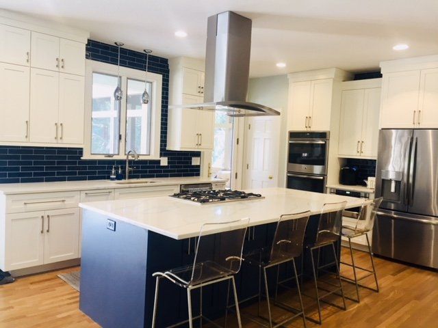 Modern white kitchen with navy island, stainless steel appliances, and four bar stools