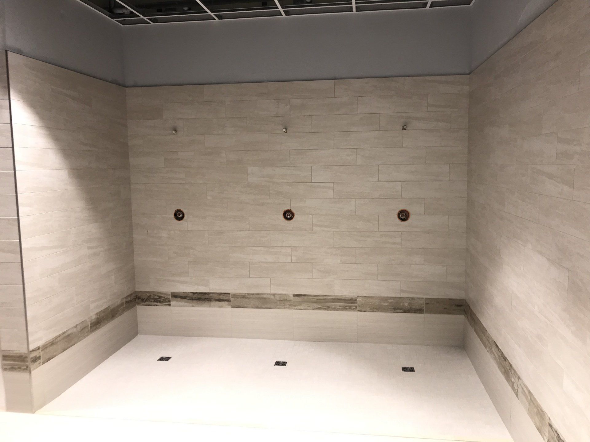 Empty tiled shower stall with beige walls, white floor, and multiple shower fixtures.