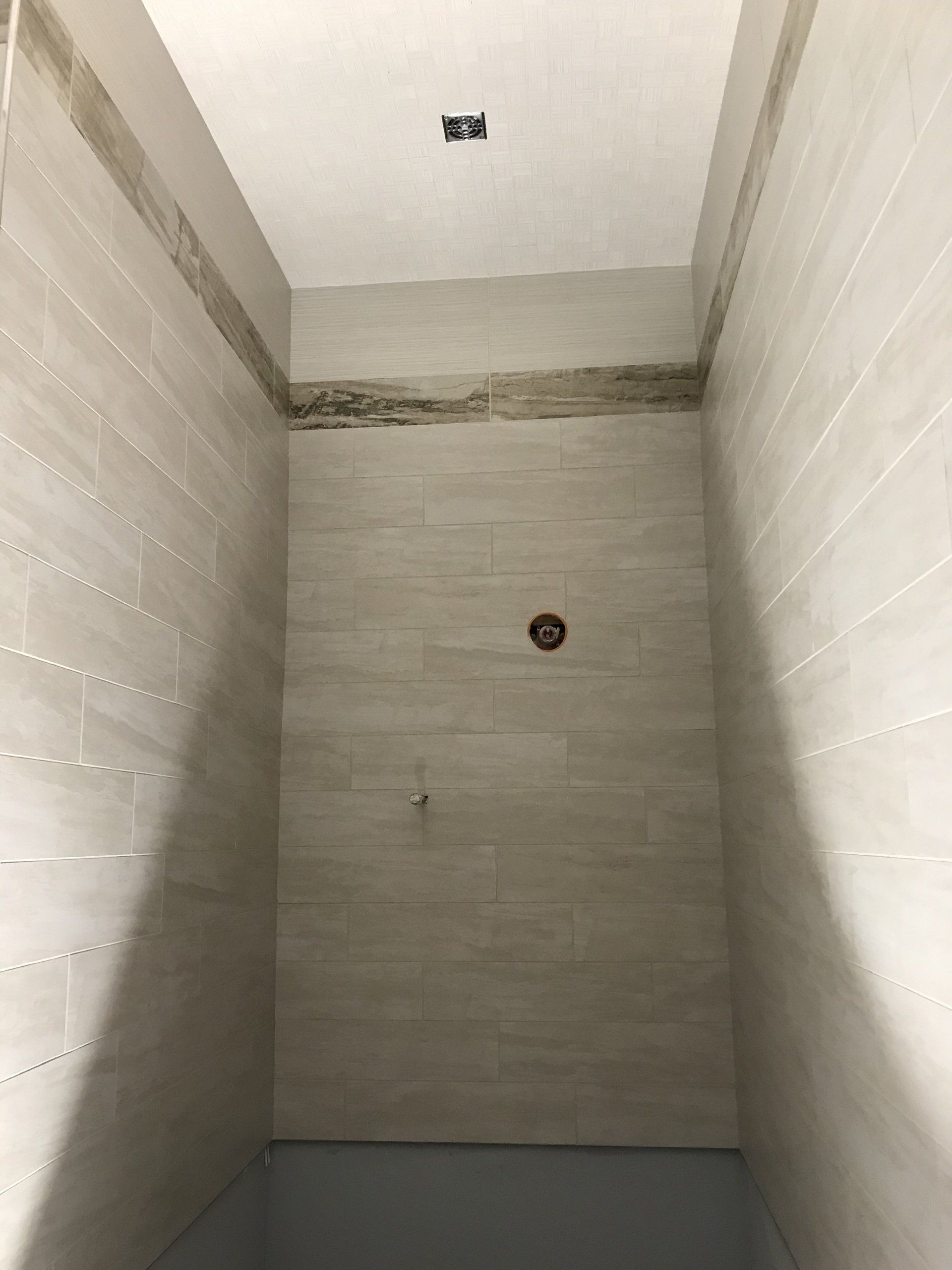 Empty tiled shower stall with white walls and a drain near the center floor.
