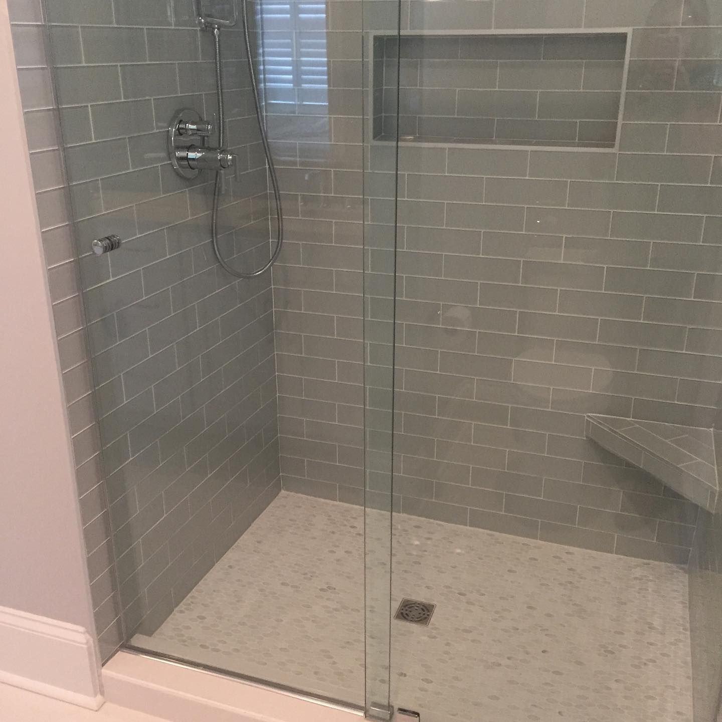 Glass walk-in shower with gray tile walls, built-in shelf, and a handheld showerhead