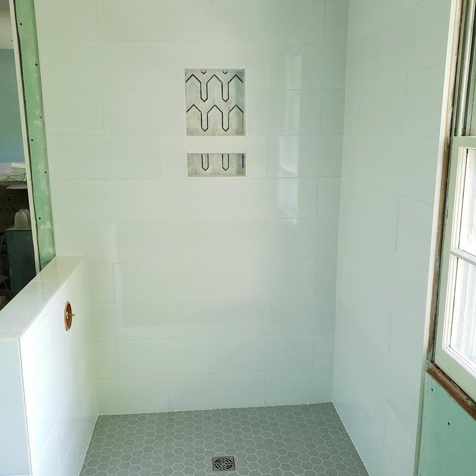 Small tiled shower stall with a drain, wall niches, and a windowed door.