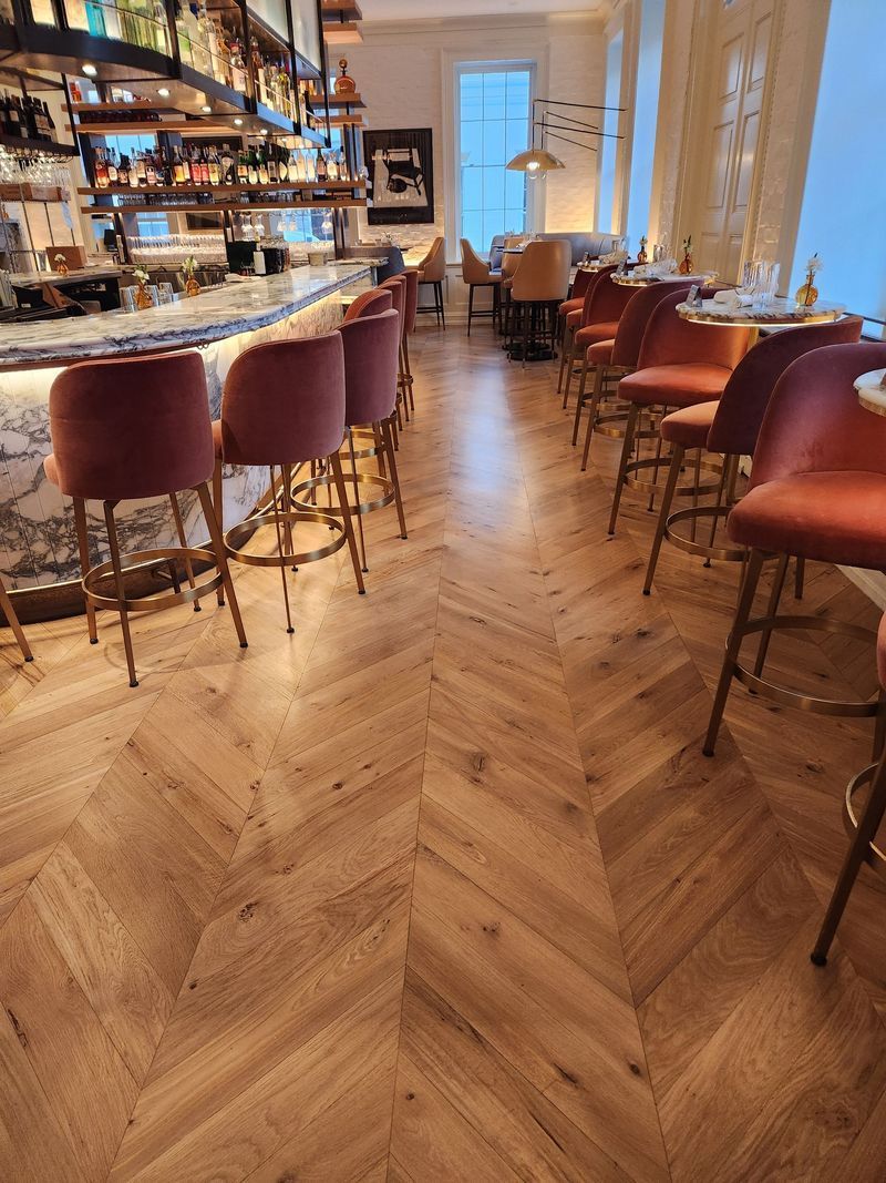 Elegant bar interior with red stools, herringbone wood floor, and warm pendant lighting