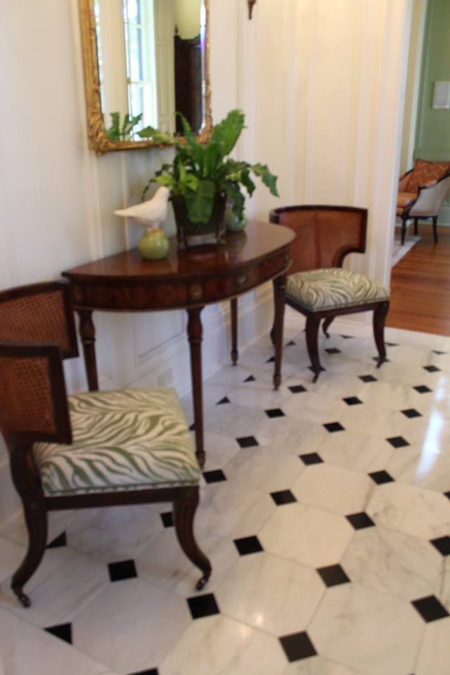Elegant hallway with a dark wood table, two chairs, a potted plant, and black-and-white tiled floor.