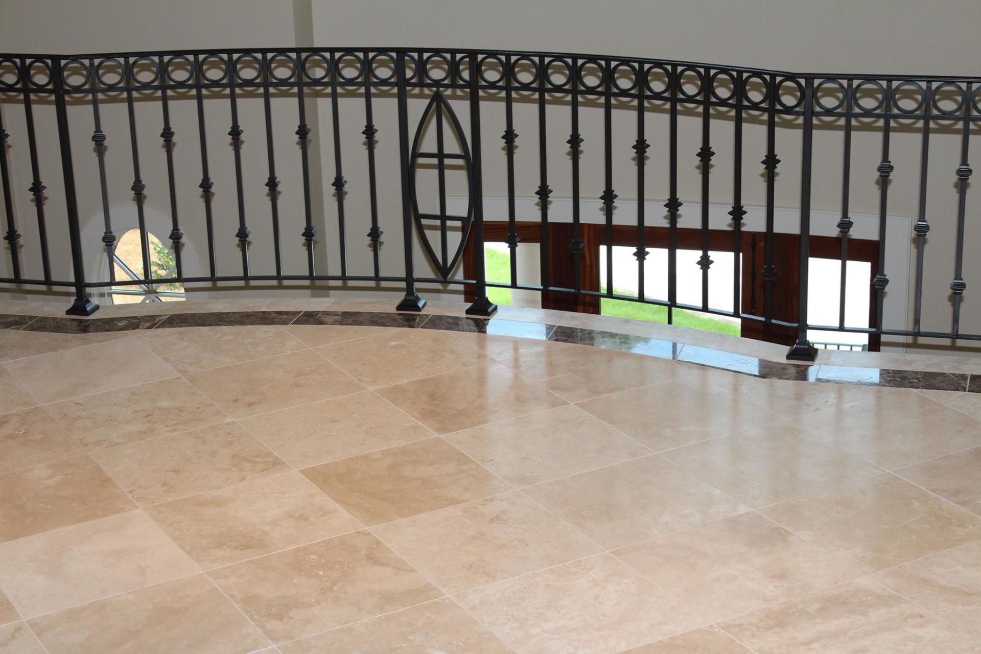 Stone balcony with ornate black railing and beige tiled floor, overlooking a lower level