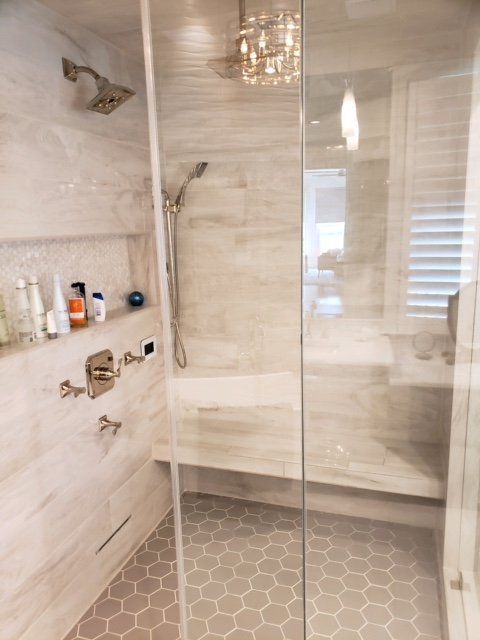 Modern shower with glass enclosure, beige tile walls, built-in shelf, and hexagon tile floor