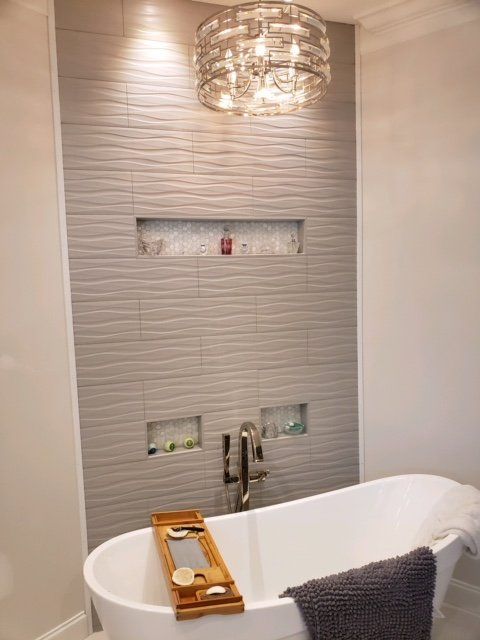 Modern bathroom with tiled shower wall, glass shelves, and a freestanding white tub under a chandelier