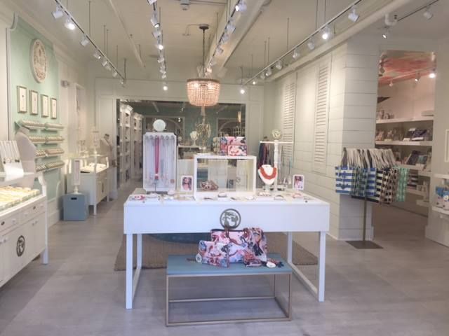 Bright white boutique interior with display tables, jewelry, and handbags under pendant lights
