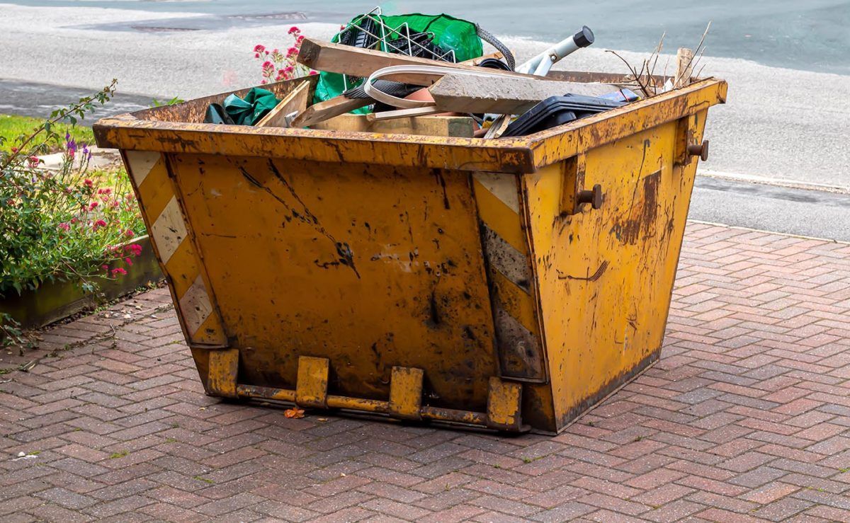A yellow dumpster filled with trash is sitting on a brick sidewalk. — Demco In Currumbin Waters, QLD