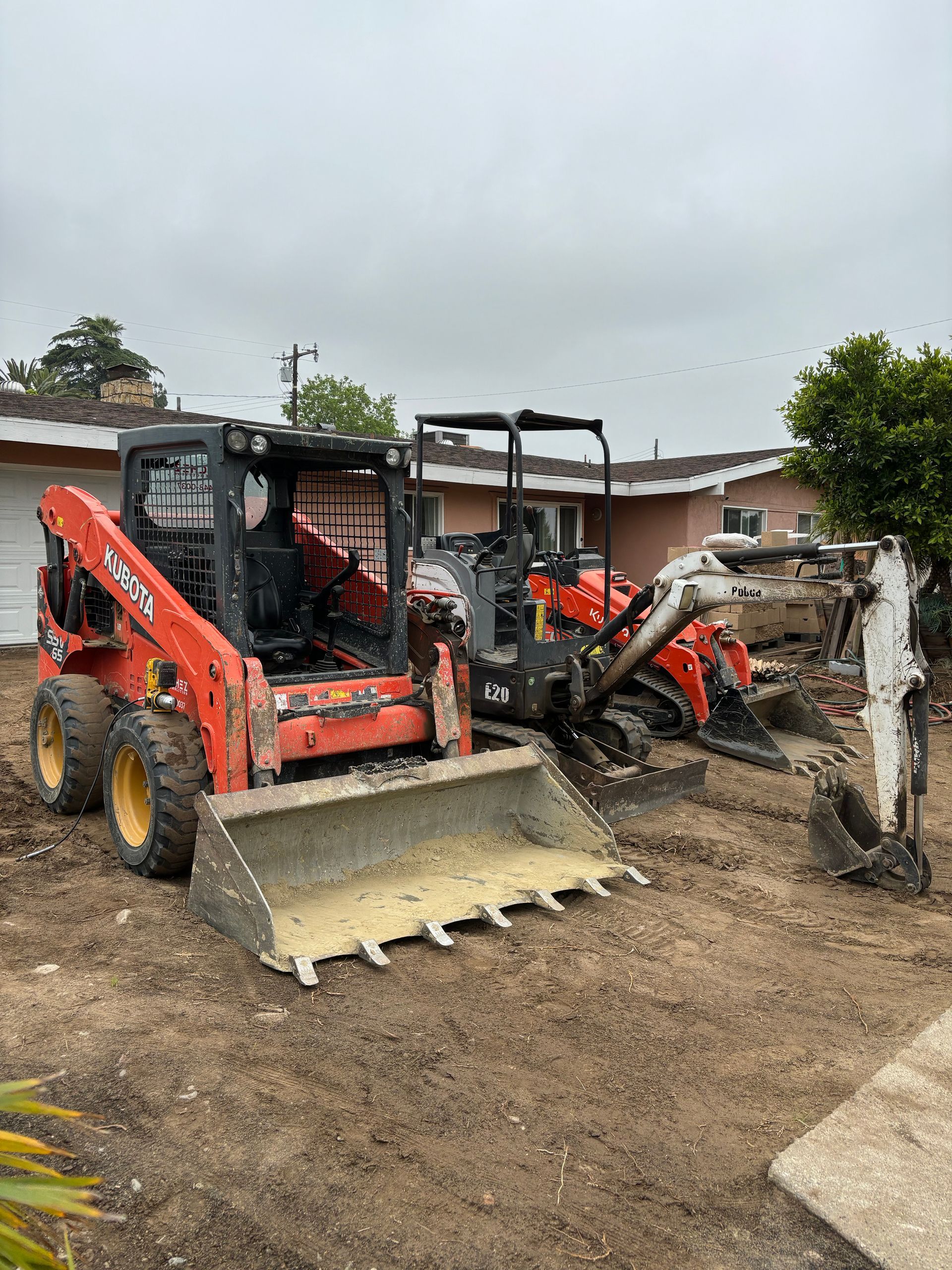 Two orange skid-steer loaders on a dirt lot beside a partially demolished building