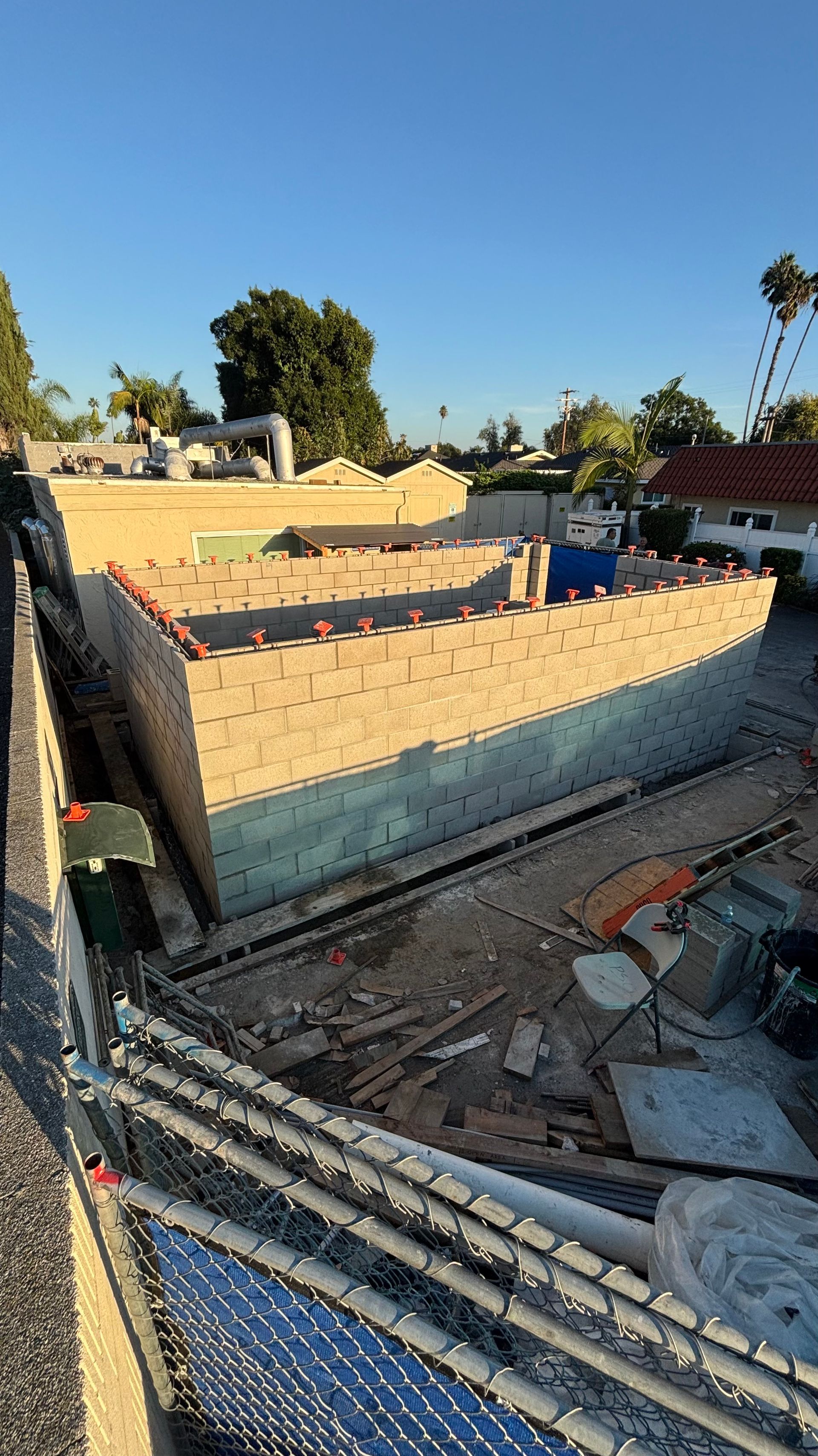 Partially built brick wall on a construction site under a clear blue sky, with tools and debris nearby