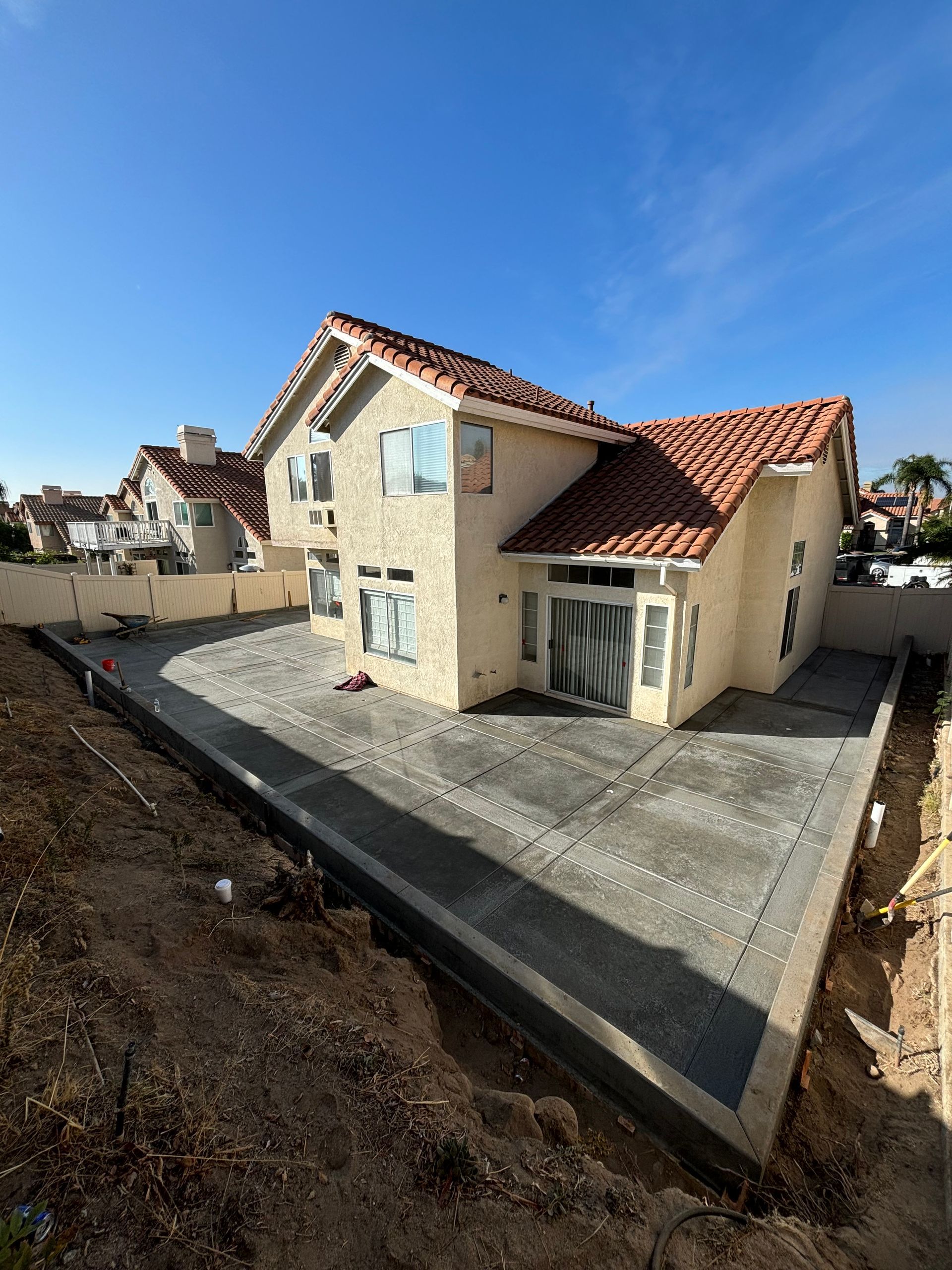 New beige house with red tile roof and concrete patio in a fenced yard under construction