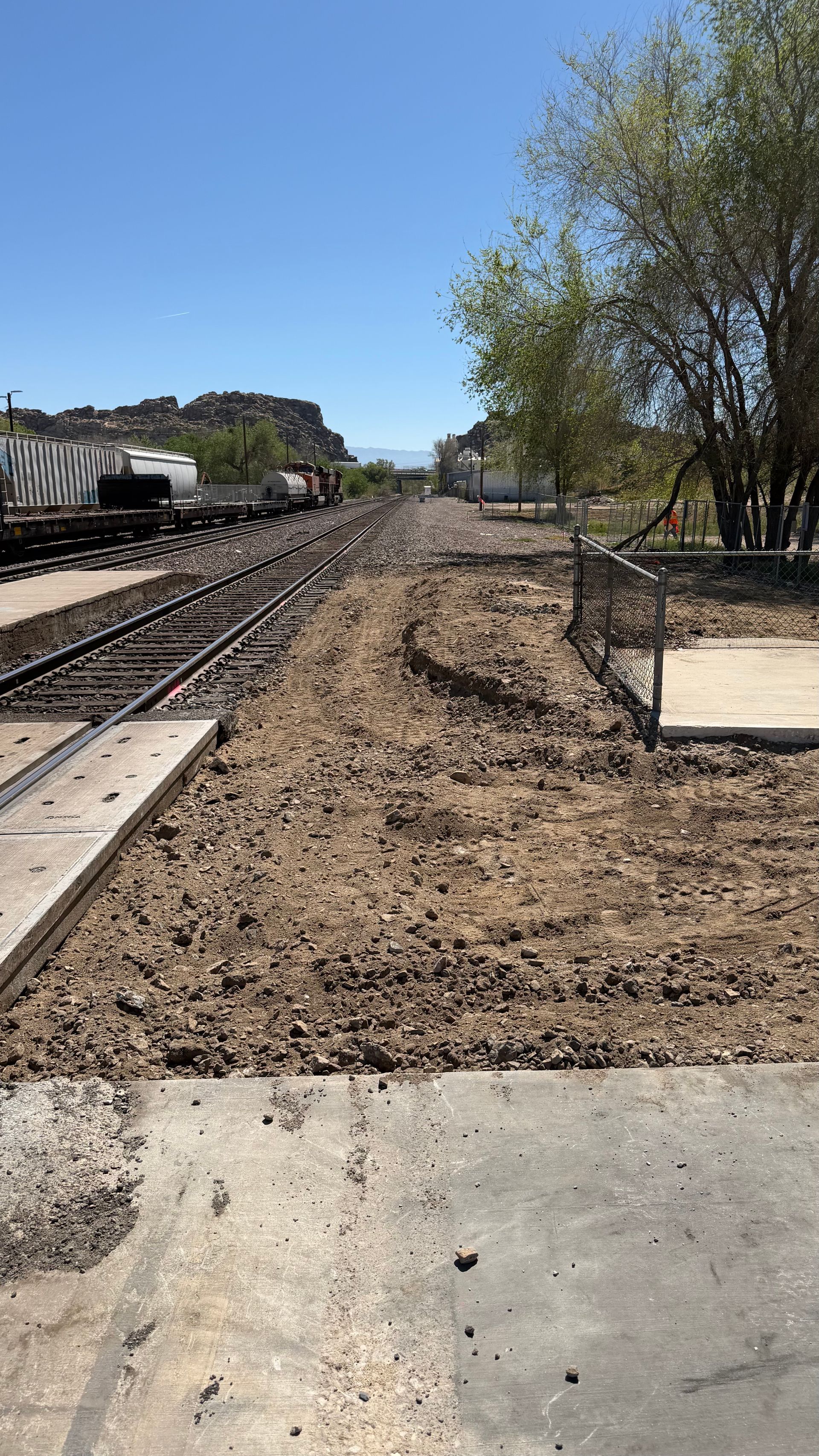 Railroad tracks beside a muddy construction area under a clear blue sky