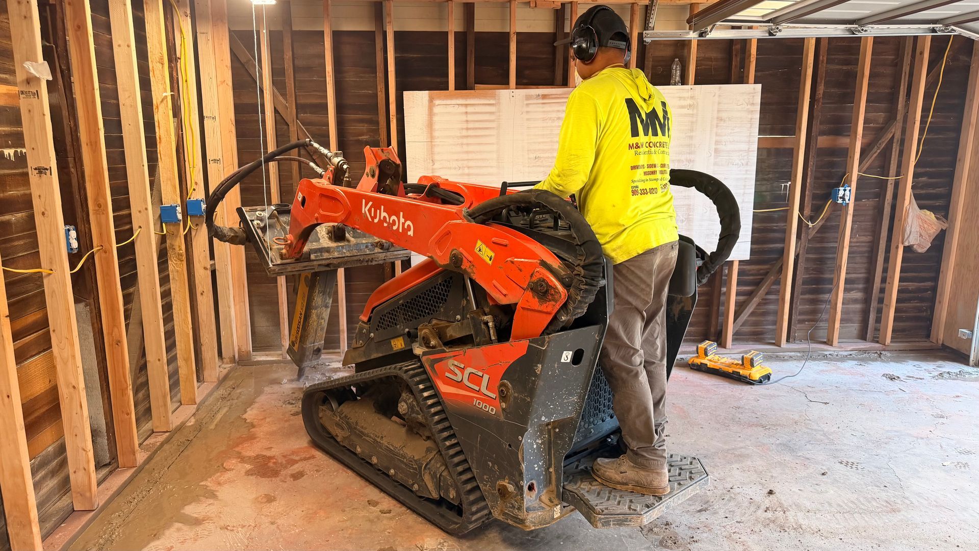 Worker operating an orange mini excavator inside a framed house under construction