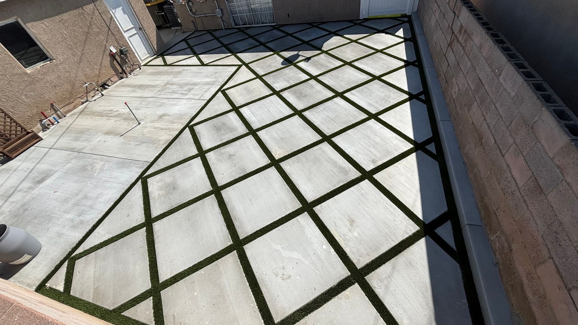 Backyard patio with concrete pavers and dark grid seams between tan brick walls