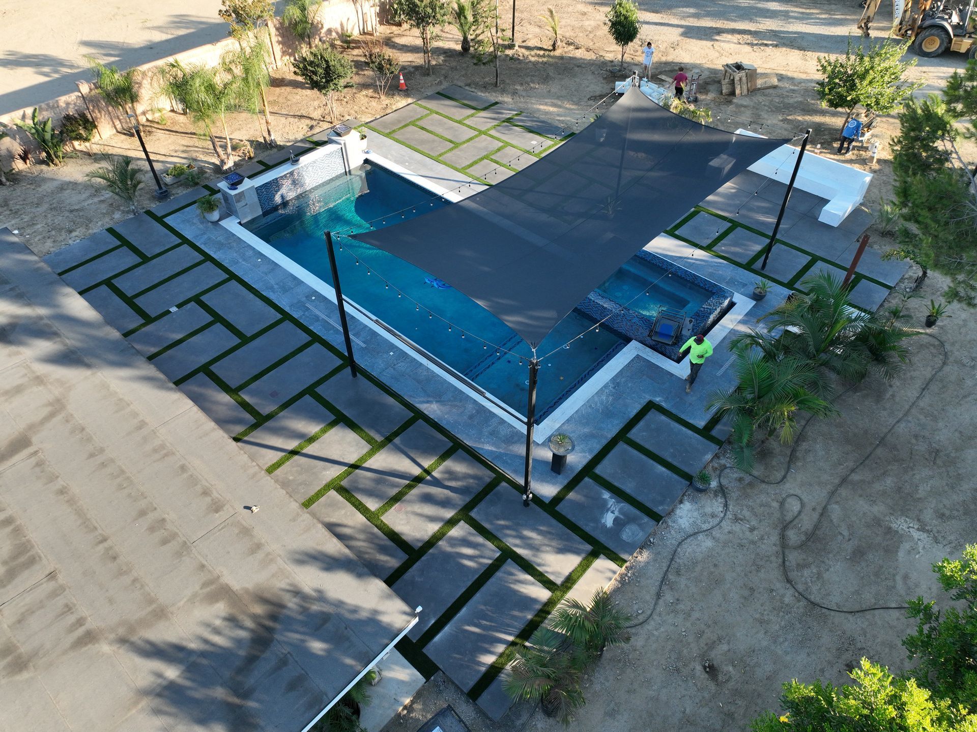 Outdoor swimming pool with a blue cover, surrounded by black pavers and desert landscaping.