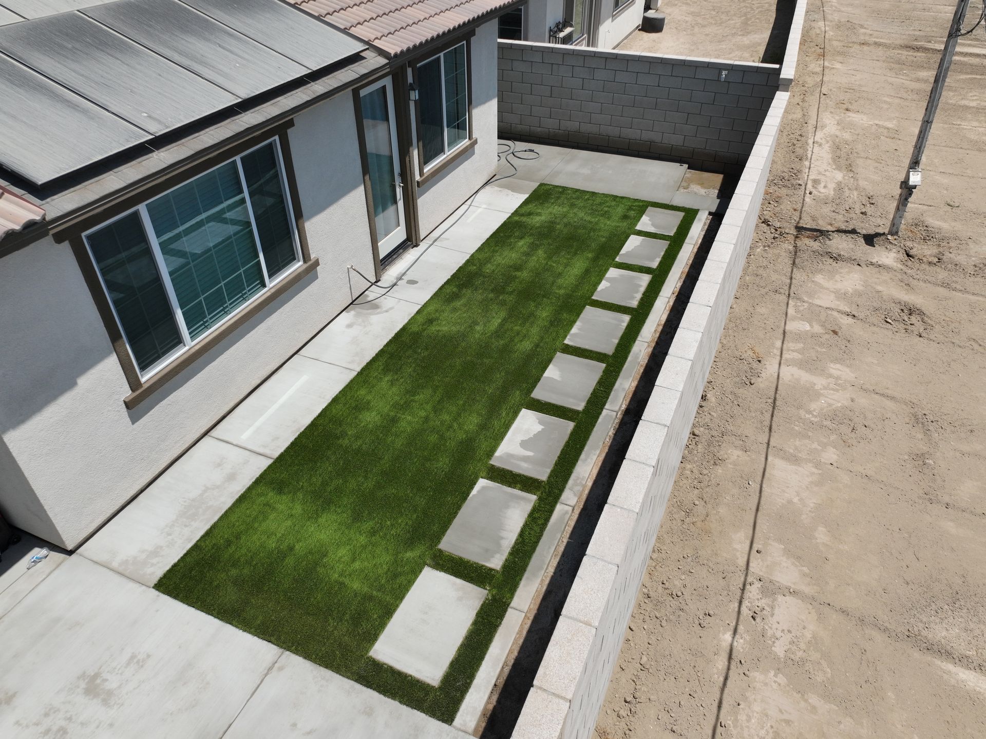 Modern house beside a narrow green lawn with stepping stones and concrete walkways