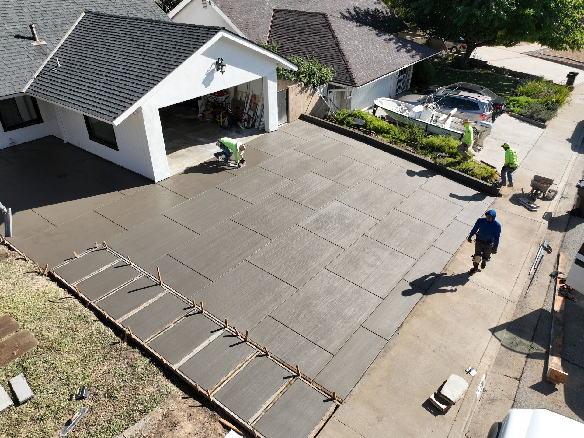 Roofing workers installing concrete pavers on a driveway beside a house and parked cars