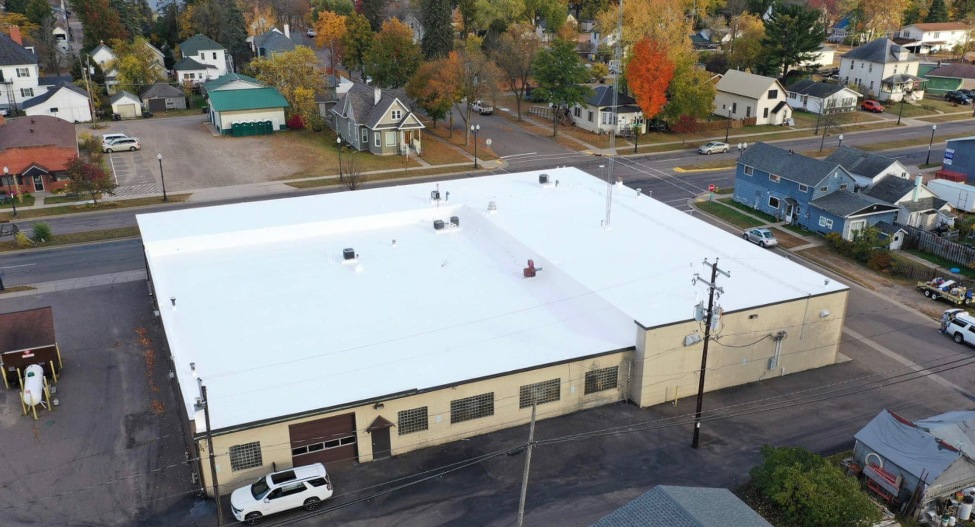Aerial view of a large, white-roofed building in a small town, surrounded by other buildings and fall foliage.