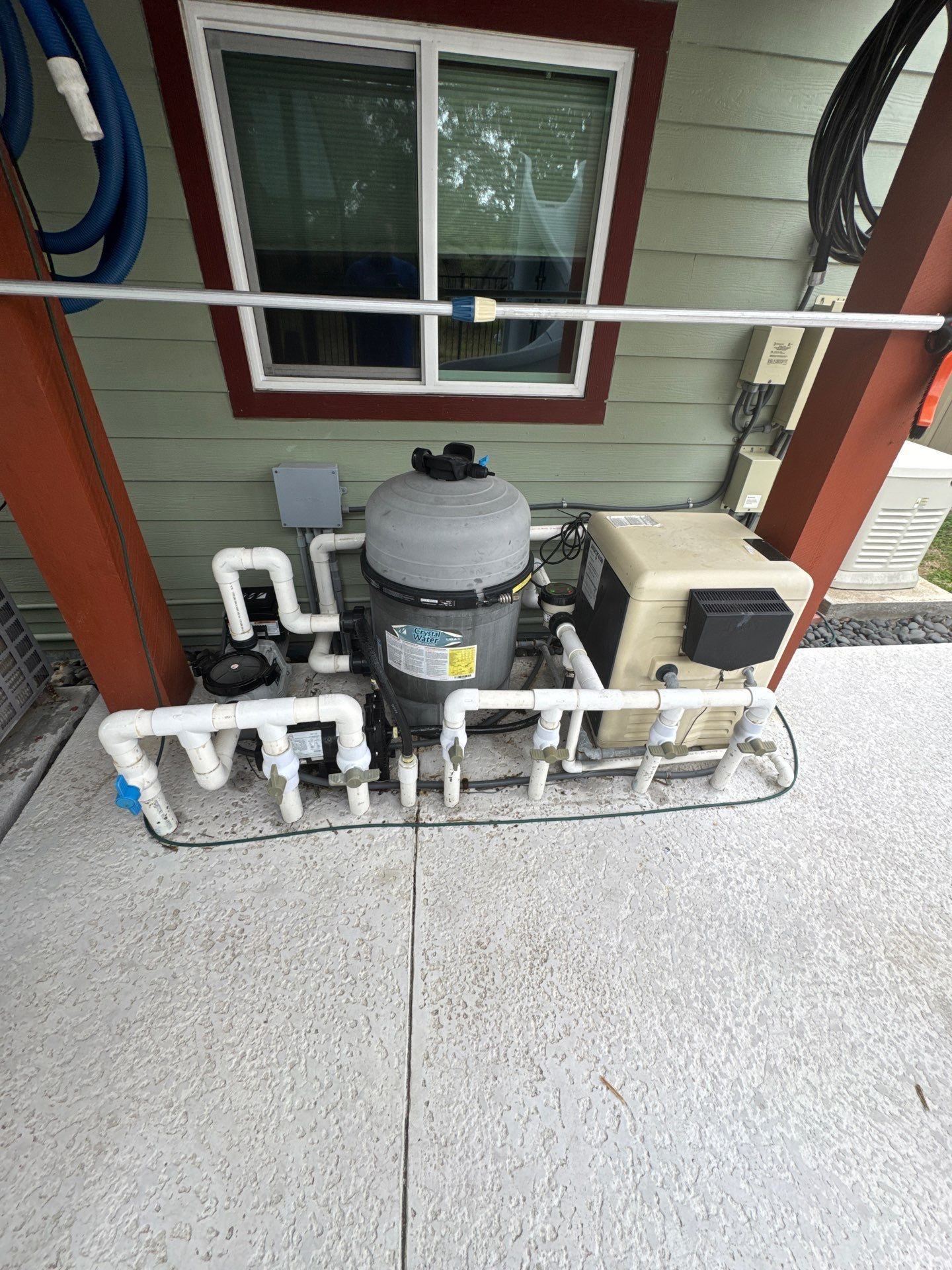 Pool equipment, including a filter and heater, on a concrete pad. Pipes and electrical wiring are visible.