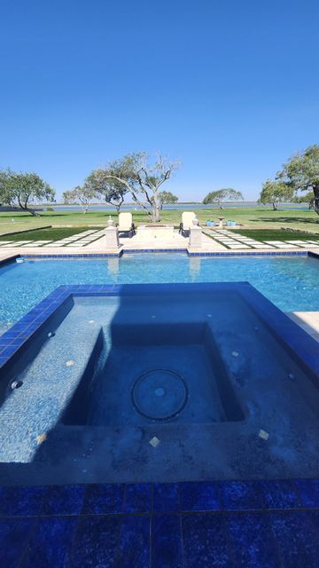 Blue tiled pool and jacuzzi with lawn and trees under a clear blue sky.