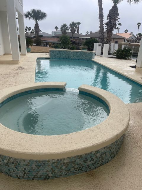 Pool area with a circular jacuzzi, a long narrow pool, and a rectangular pool, all light blue and surrounded by light stone.