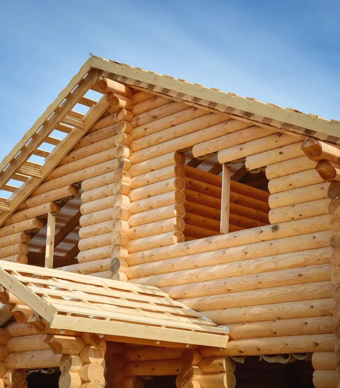 Partially built log cabin with unfinished roof and window openings against a blue sky