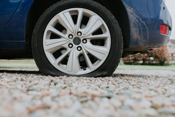 Blue car with a flat tire on a gravel driveway.