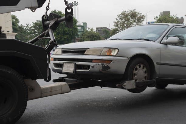 Silver car being towed by a black tow truck, front wheels off the ground.