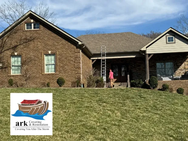 Brick house with a ladder at the front entry and a person in a pink jacket on the porch, under a blue sky