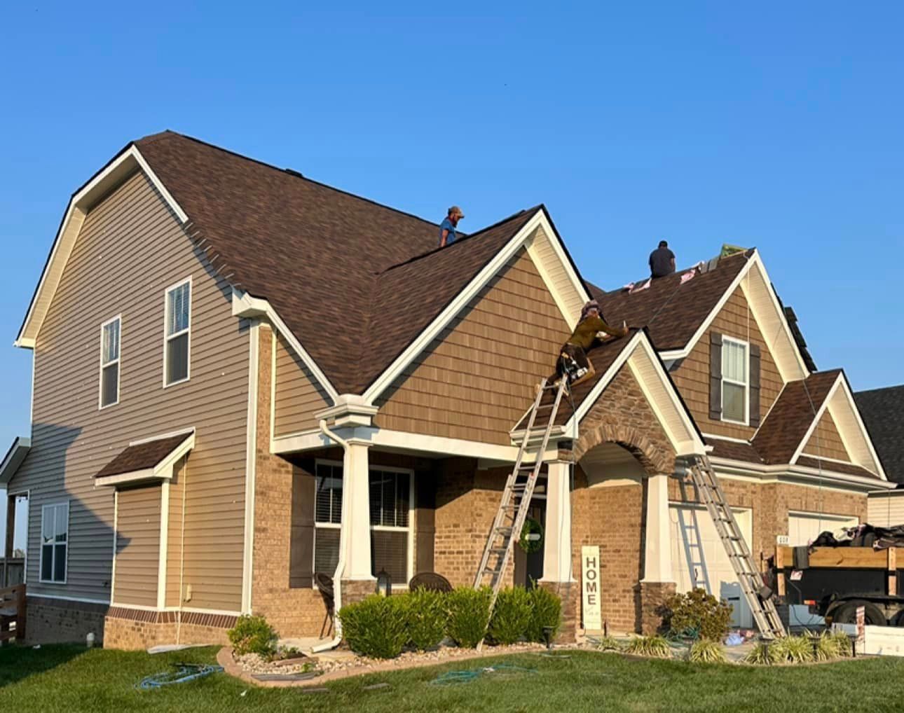 A large brick house with a brown roof is being painted.
