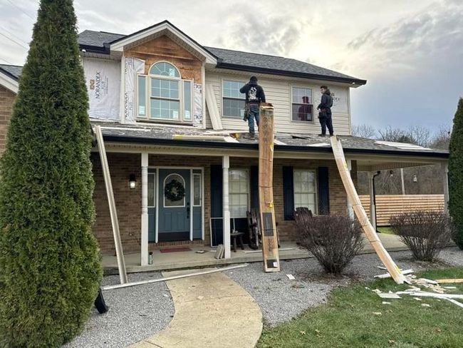 Two workers on a ladder installing siding on a two-story house with scaffolding.