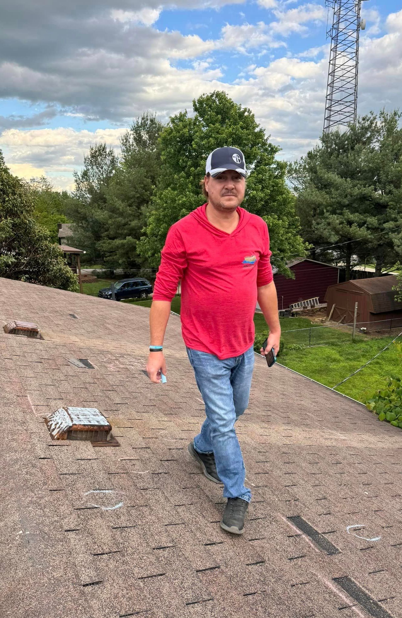 Man in a red shirt walking on a rooftop with trees and cloudy sky behind him