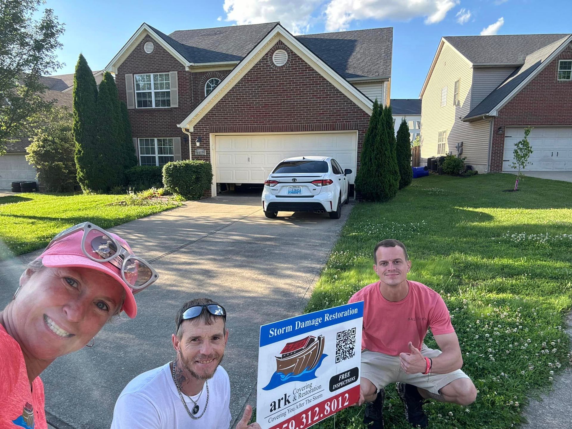 A group of people are standing in front of a house holding a sign.