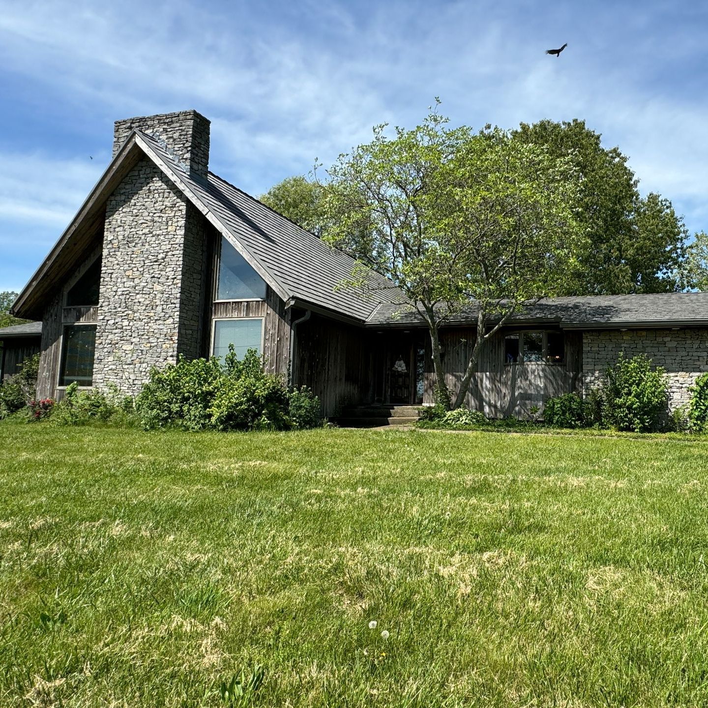 Stone house with a steep roof and large lawn under a blue sky