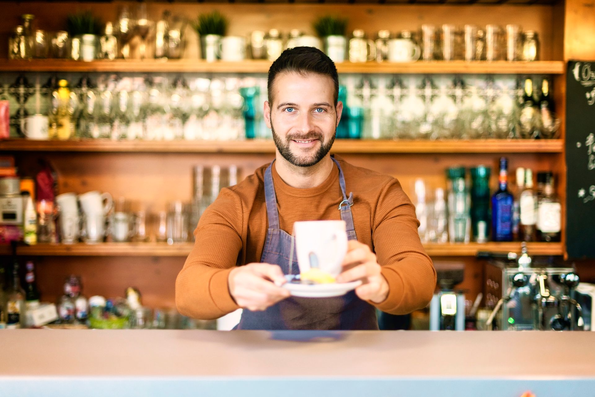 Smiling male teahouse owner standing behind the counter and offering a hot tea. Smiling male teahouse owner standing behind the counter and offering a hot tea.