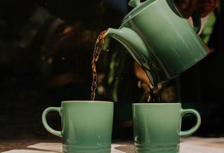 Green teapot pouring tea into two green mugs.