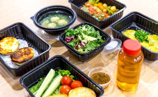 Prepared meals in black containers: soup, salad, side dishes, dressing, juice.