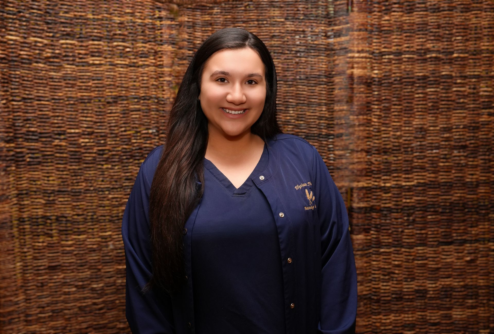 Smiling person in a navy shirt standing against a woven brown backdrop
