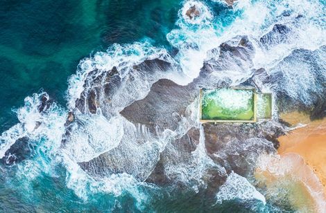 Aerial view of waves crashing onto a turquoise beach beside a small green-roofed structure
