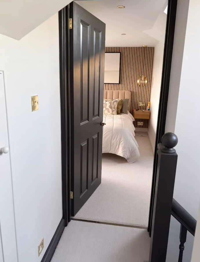 A bedroom with a bed and a black door leading into the master bedroom of a new loft space.